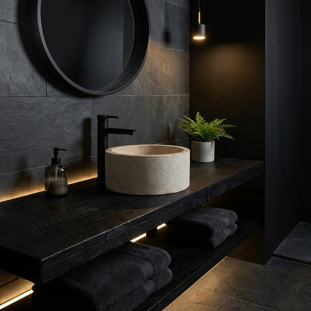 Pyöreä työtasoinen pesuallas elegantilla marmorilla tummalla puukonsolilla, lavastettu minimalistiseen tummaan tunnelmaan.