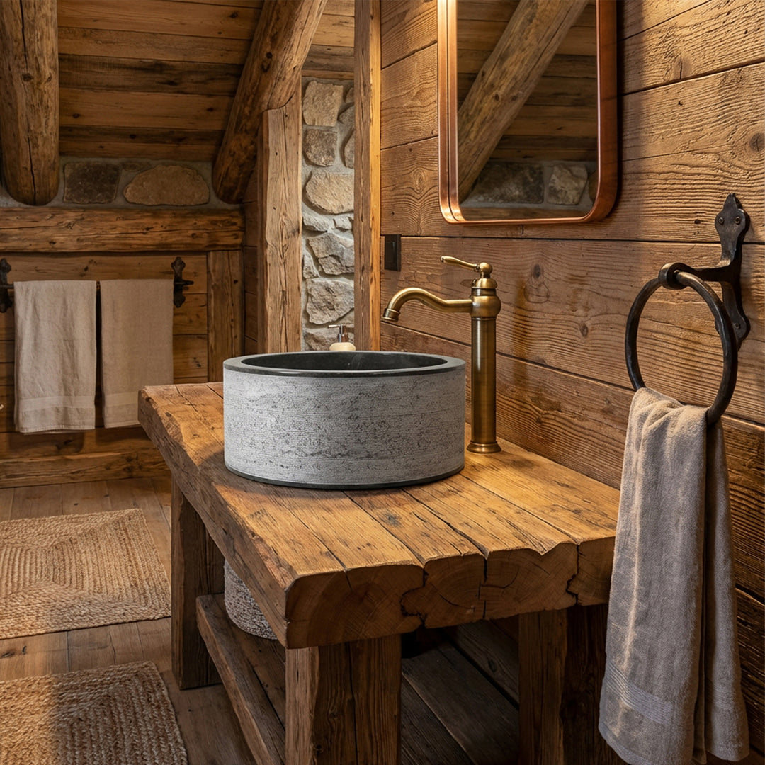 Pyöreä työtasoinen kivestä valmistettu pesuallas massiivipuupöydällä yhdistettynä messinkikalusteisiin maalaismaisessa chalet-kylpyhuoneessa.